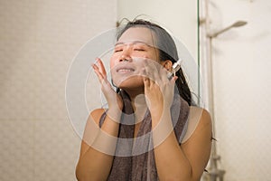 Young beautiful and happy Asian Korean woman applying serum facial skin care and face treatment in the bathroom enjoying morning photo