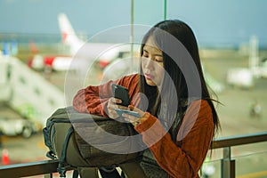 Young beautiful and happy Asian Korean woman checking mobile phone holding passport in her hand at airport departure lounge