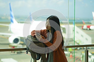 Young beautiful and happy Asian Korean woman checking mobile phone holding passport in her hand at airport departure lounge