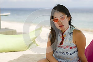 Young beautiful and happy Asian Korean woman in chic Summer dress and hipster sunglasses posing relaxed at tropical beach relaxed