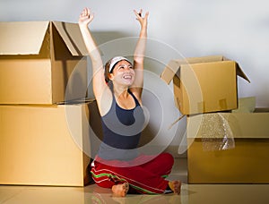 Young beautiful and happy Asian Korean woman excited at home living room floor unpacking belongings from cardboard boxes moving to