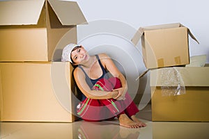 Young beautiful and happy Asian Korean woman excited at home living room floor unpacking belongings from cardboard boxes moving to