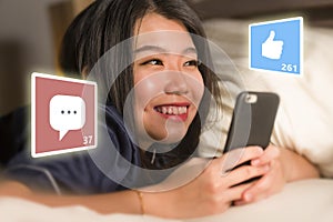 Young beautiful and happy Asian Korean woman in pajamas using mobile phone social media smiling cheerful lying on bed at home