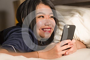 Young beautiful and happy Asian Korean woman in pajamas using mobile phone social media texting with her boyfriend or enjoying