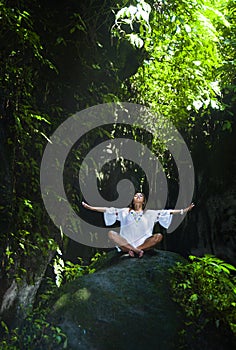 Young beautiful and happy Asian practicing yoga outdoors at amazing peaceful and fresh tropical background sitting in rock doing r