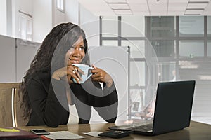 Young beautiful and happy black African American business woman working at office computer desk drinking coffee smiling cheerful