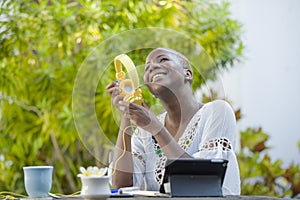 Young beautiful and happy black African American woman enjoying outdoors at cafe working with digital tablet listening to music wi