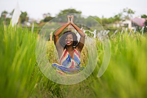 Young beautiful and happy black African American woman sitting at rive field outdoors practicing yoga relaxation and meditation