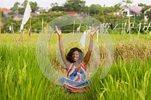 Young beautiful and happy black afro American woman sitting at rive field outdoors practicing yoga relaxation and meditation