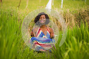 Young beautiful and happy black afro American woman sitting at rive field outdoors practicing yoga relaxation and meditation