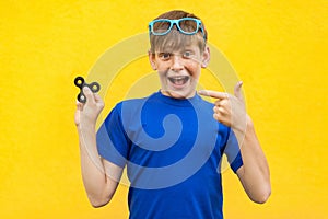 Young beautiful happy boy with freckles blue t-shirt holding fidget spinner on yellow background