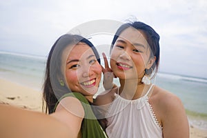 Young beautiful and happy couple of attractive Asian Korean women at the beach enjoying holidays having fun taking selfie together