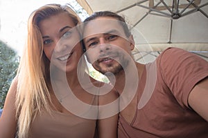 A young beautiful happy couple sitting in a cafe outside and making selfie ,