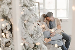 Young beautiful happy couple, sitting on the couch near the Christmas tree.