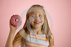 Young beautiful happy and excited blond girl 8 or 9 years old holding donut desert on her hand looking spastic and cheerful in sug