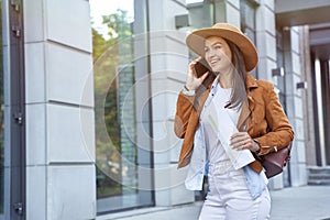 Young and beautiful happy female traveler or tourist wearing hat and backpack holding map and talking by phone with