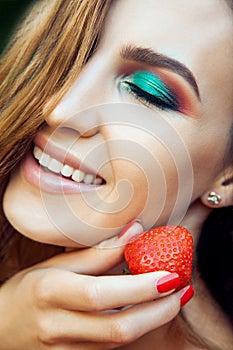 Young beautiful happy funny girl with red dress and makeup holding strawberry in summertime in the park.