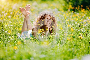 Young beautiful happy girl on the grass. Smiling curly woman in a sunny meadow. Positive model in a blue dress. Summer scene