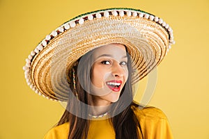 Young beautiful happy girl in sombrero isolated over yellow background.