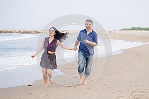 Young beautiful and happy mixed ethnicity couple of Asian woman and Caucasian man relaxed and cheerful running playful  on beach