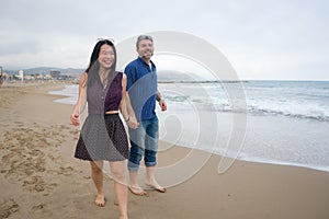 Young beautiful and happy mixed ethnicity couple of Asian woman and Caucasian man relaxed and cheerful walking playful  on beach