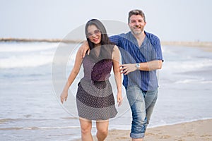 Young beautiful and happy mixed ethnicity couple of Asian woman and Caucasian man relaxed and cheerful walking playful  on beach