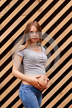 Young beautiful and happy pregnant girl on a striped background. Second trimester Holds his hands on his stomach. Vertical photo.