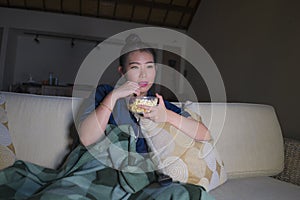 Young beautiful happy and relaxed Asian Korean woman at home living room sitting cozy on sofa couch watching TV show episode or