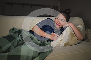 Young beautiful happy and relaxed Asian Korean woman at home living room sitting cozy on sofa couch watching TV show episode or