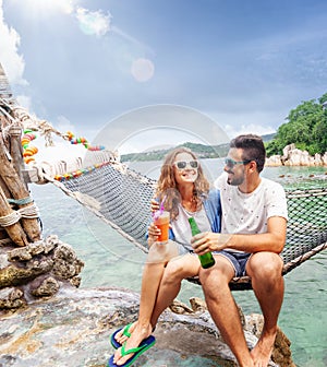 Young beautiful happy smiling funny couple a man and a woman best friends on a hammock on vacation drink refreshing drinks