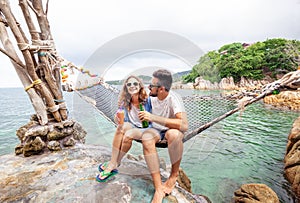 Young beautiful happy smiling funny couple a man and a woman best friends on a hammock on vacation drink refreshing drinks