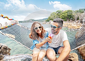 Young beautiful happy smiling funny couple a man and a woman best friends on a hammock on vacation drink refreshing drinks