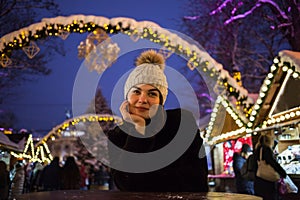 Young beautiful happy smiling girl posing in street. Festive Christmas fair on background