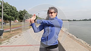 Young beautiful happy sporty fitness woman standing near the river stretching her muscles preparing for jogging and running