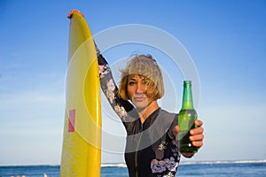 Young beautiful and happy surfer woman holding yellow surf board smiling cheerful drinking beer bottle enjoying summer holida