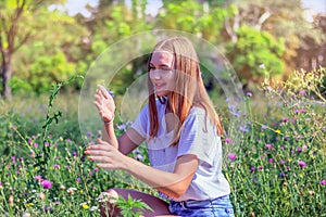 Young beautiful happy teenage girl sitting on a meadow among flowering plants and holding a ladybug in her hands, female portrait