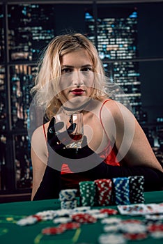 young beautiful happy woman inred dress holds her cards pair of aces and chips on green background