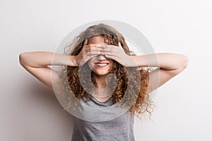 Young beautiful happy woman in studio, covering her eyes.