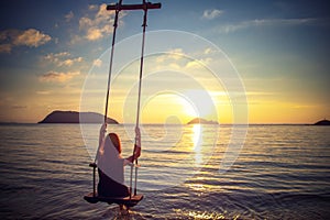 Young beautiful happy woman swinging on a swing on the beach during sunset, relaxing travel lifestyle concept