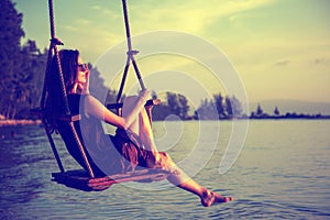 Young beautiful happy woman swinging on a swing on the beach during sunset, relaxing travel lifestyle concept