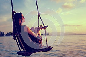 Young beautiful happy woman swinging on a swing on the beach during sunset, relaxing travel lifestyle concept