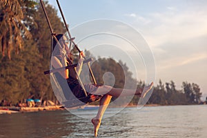 Young beautiful happy woman swinging on a swing on the beach during sunset, relaxing travel lifestyle concept