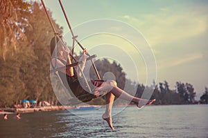 Young beautiful happy woman swinging on a swing on the beach during sunset, relaxing travel lifestyle concept