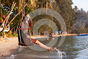 Young beautiful happy woman swinging on a swing on the beach during sunset, relaxing travel lifestyle concept