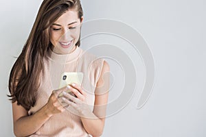 Young beautiful happy woman using smart phone. Girl texting on her mobile phone. Isolated on grey background