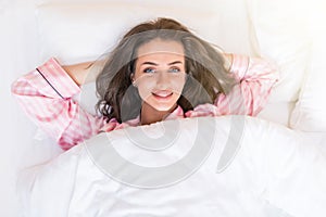 Young beautiful happy woman waking up on bed, top view