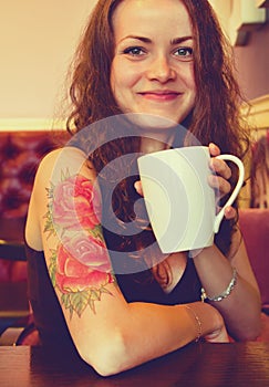 Young beautiful hipster tattooed woman with red curly hair at the bar with cup of coffee