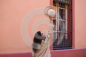 Young and beautiful Hispanic brunette woman with curly hair holds up a hat with her hand while making different expressions and