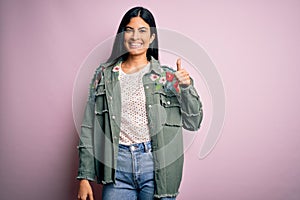 Young beautiful hispanic fashion woman wearing cool jacket over pink background doing happy thumbs up gesture with hand