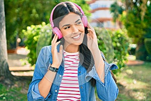 Young beautiful hispanic girl listening to music using headphones standing at the park